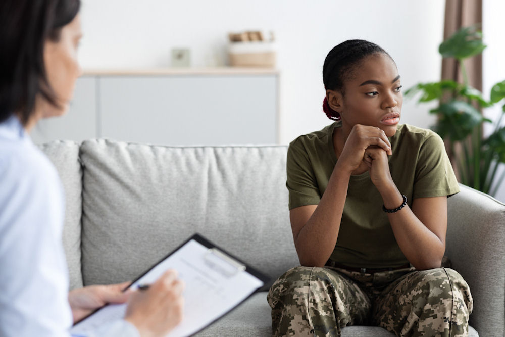 Young soldier in camouflage pants and green shirt looking away from therapist