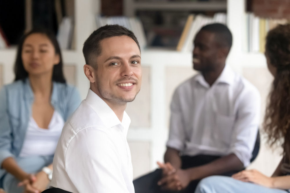 Man looking back from a mixed gender 12-step program to smile at the camera
