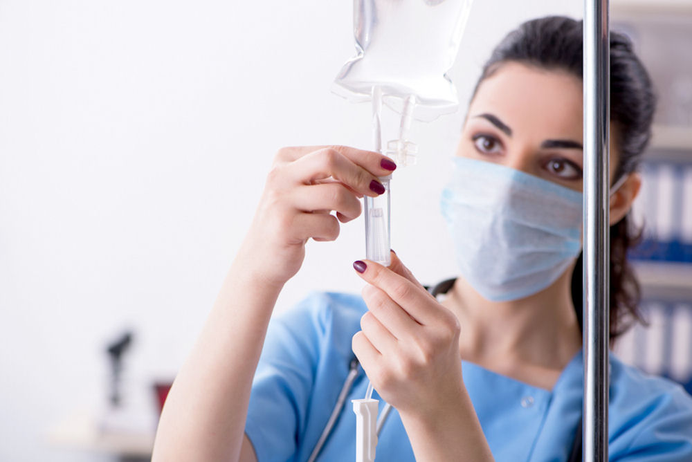 Female nurse wearing mask administering medicine through an IV