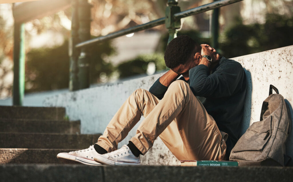 Distraught young man sitting on stone steps with hands behind his head