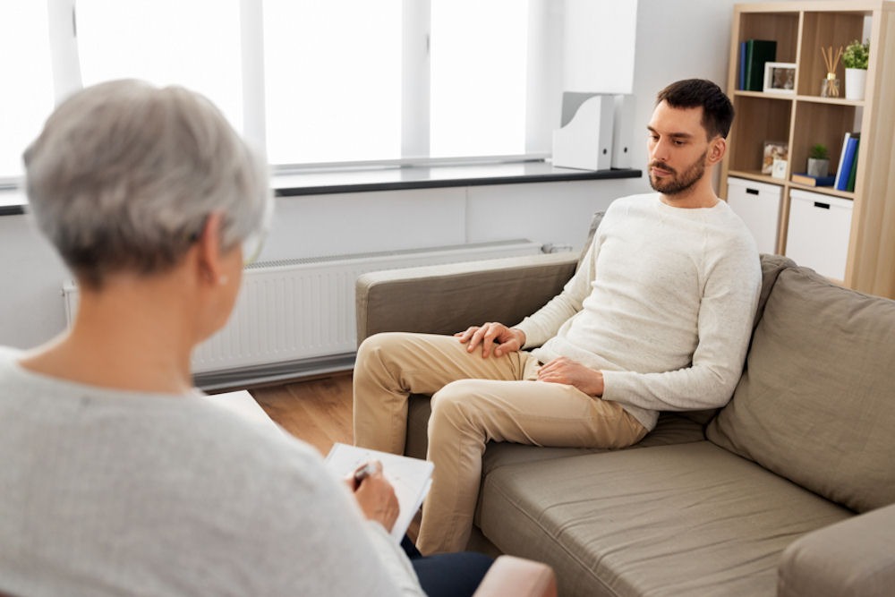 man sitting on couch discussing addiction with therapist
