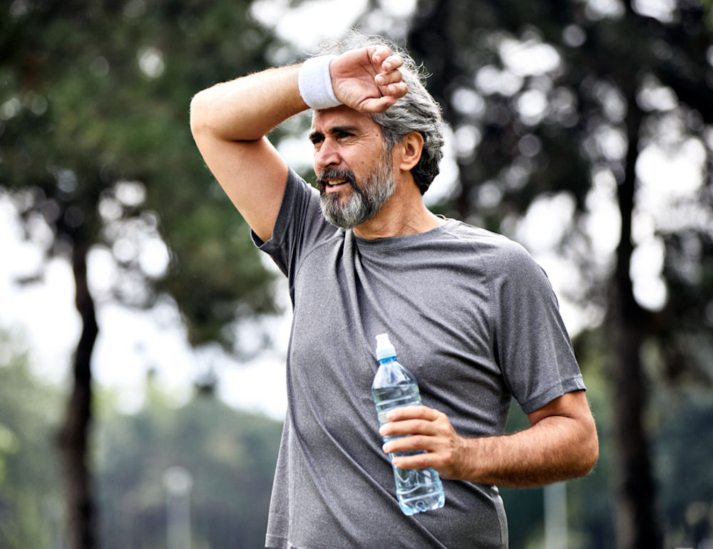 Older man pausing a run to wipe forehead and drink water