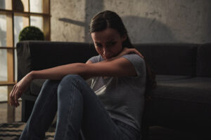 Sad young woman thinking while sitting on the floor against the couch