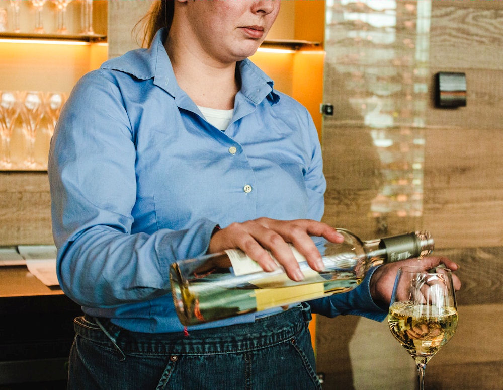 Service person pouring white wine into a glass with a sad expression