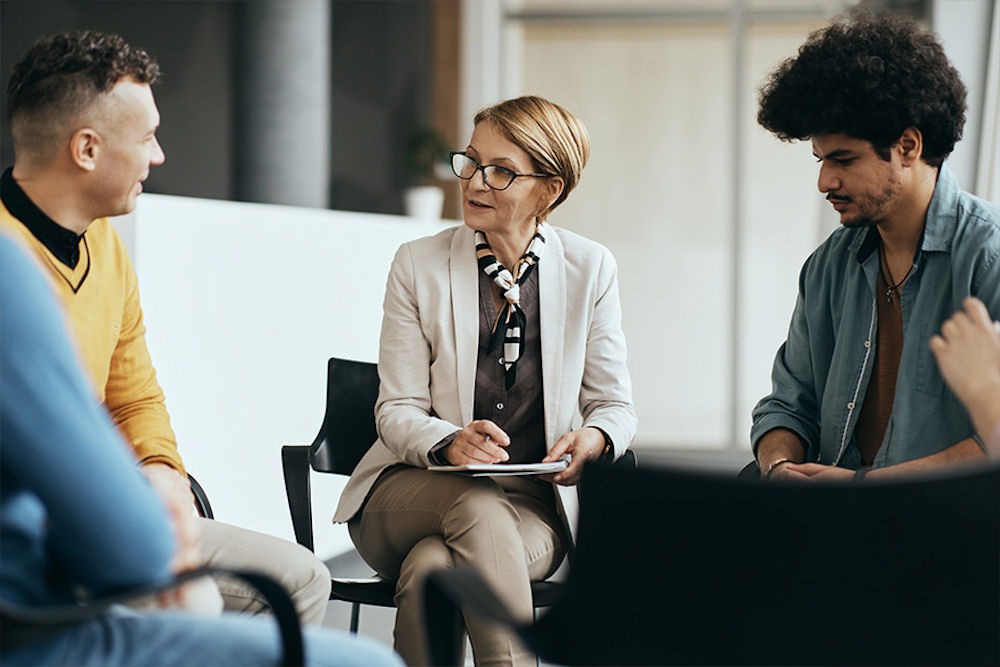 Older professional woman facilitating group while sitting between two young men
