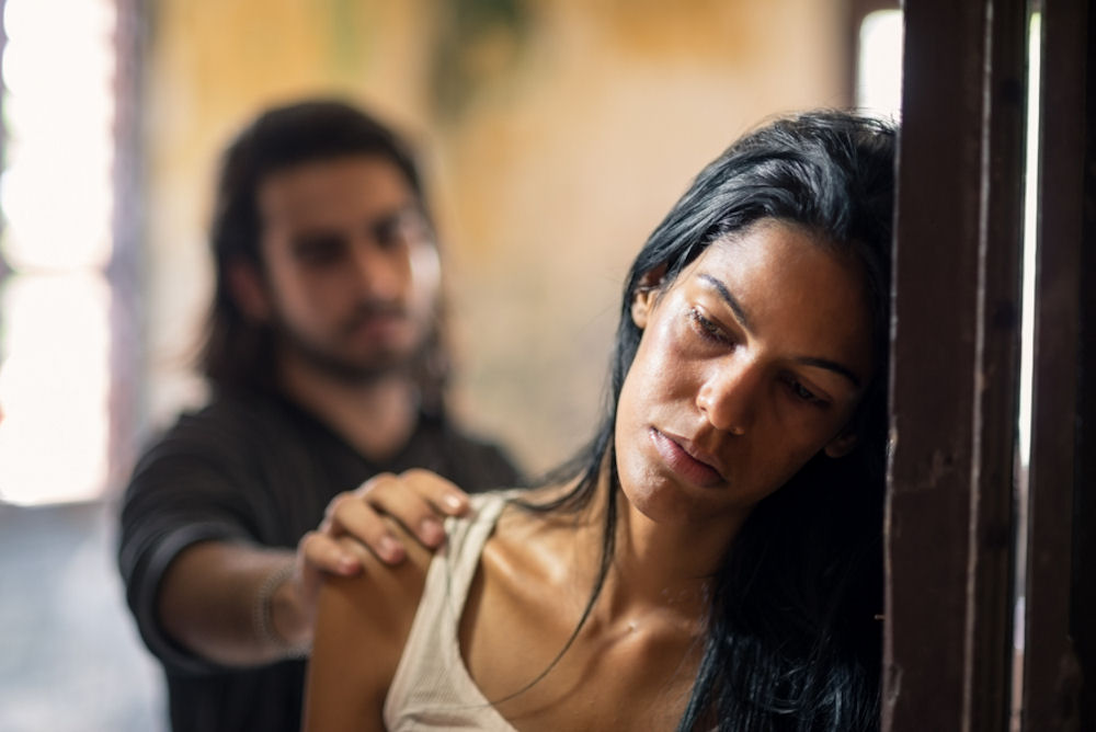 Stressed out woman leaning on doorway while man reaches out to reassure her