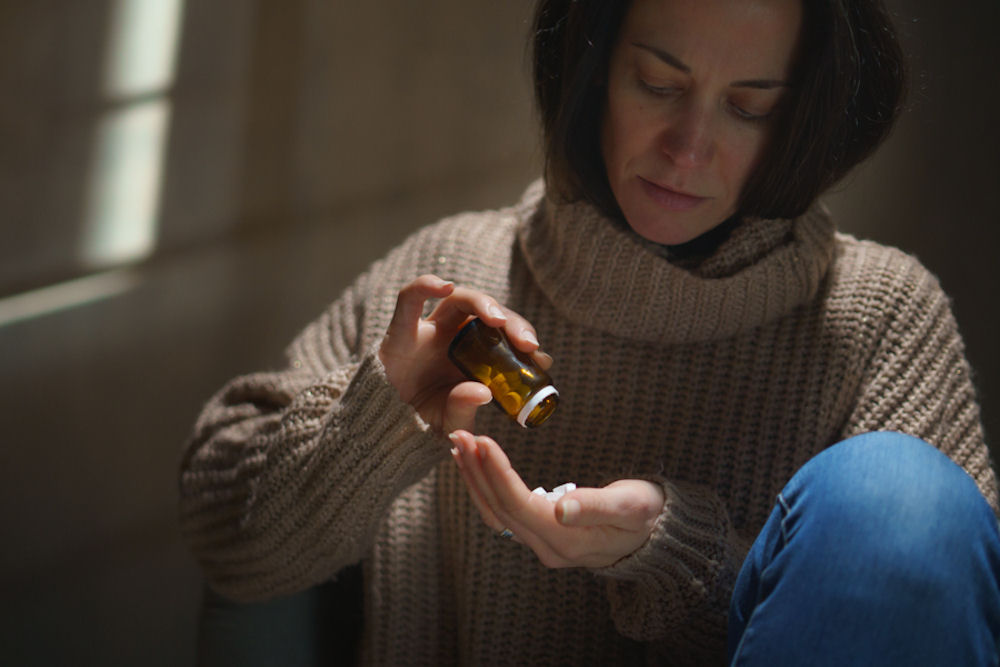 Woman wearing sweater and jeans pouring pills from a bottle into her hand