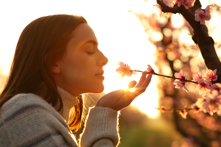 Woman in light sweater smelling flower in front of setting sun