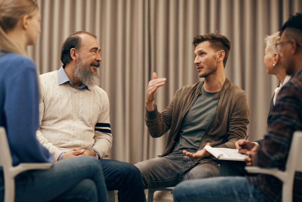 Man gesticulating while speaking in a sober living 12-step group filled with people of different ages