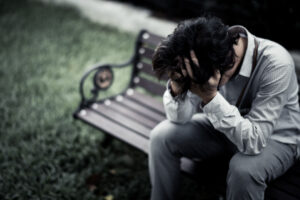 Man going through cocaine withdrawal holding his head while sitting on a park bench