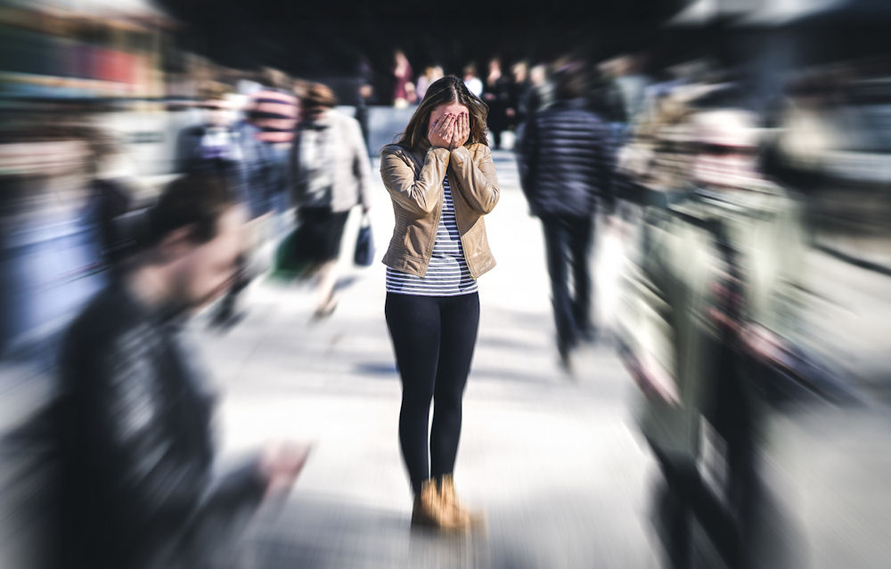 Focused shot of woman covering her face with her hands while city crowd walks around her