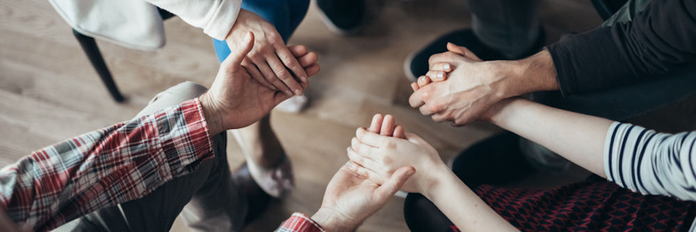Overhead shot of four people in a group therapy circle holding hands