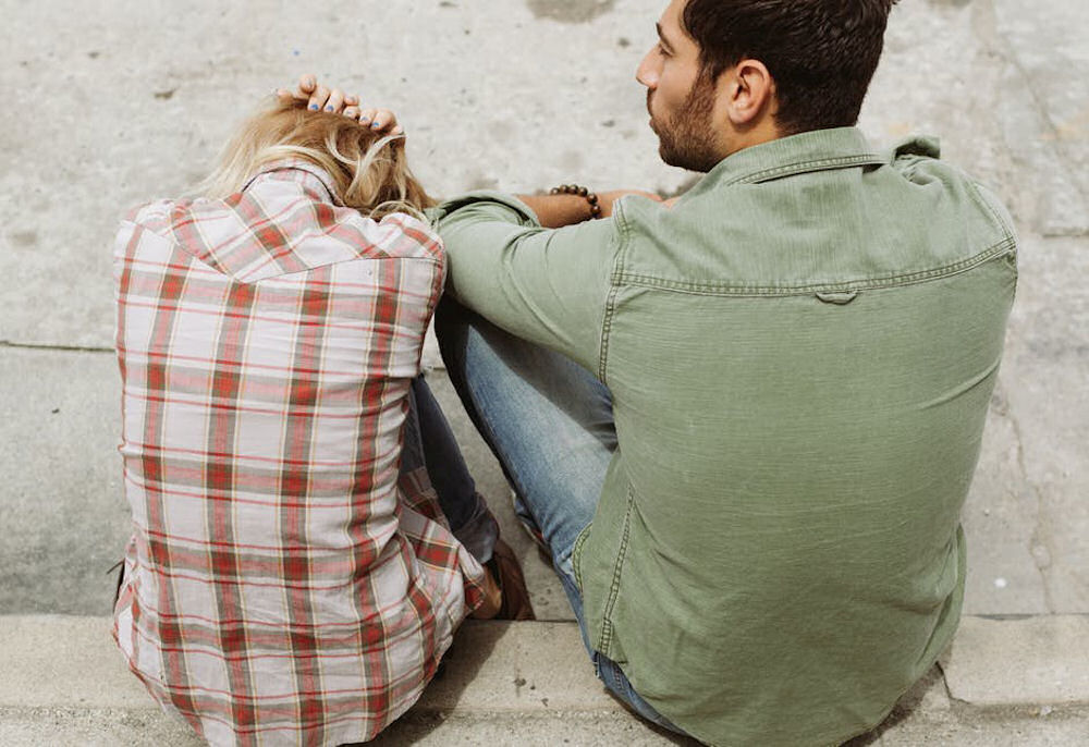 Heterosexual couple sitting on a concrete stair, with the woman clutching her head while slumped over