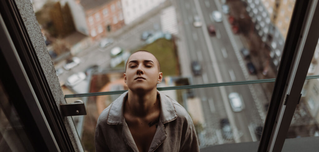 Woman in opioid addiction treatment leaning head back against window with street view