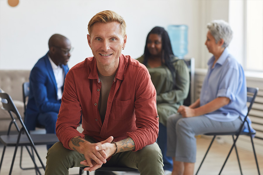 Man facing camera with addiction aftercare support group chatting in the background