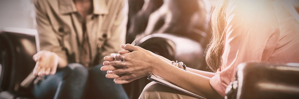 Neck-down show of a woman speaking to therapist while both sit in leather chairs