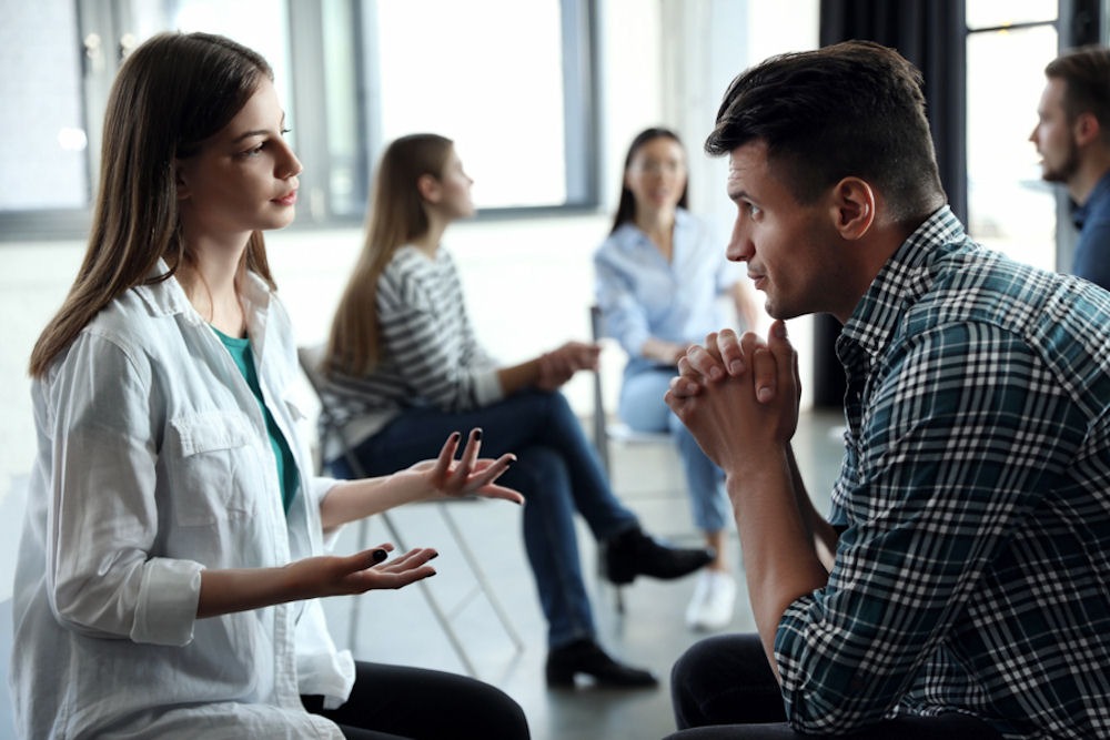 Man listening to woman speaking across from him in alcohol addiction support group