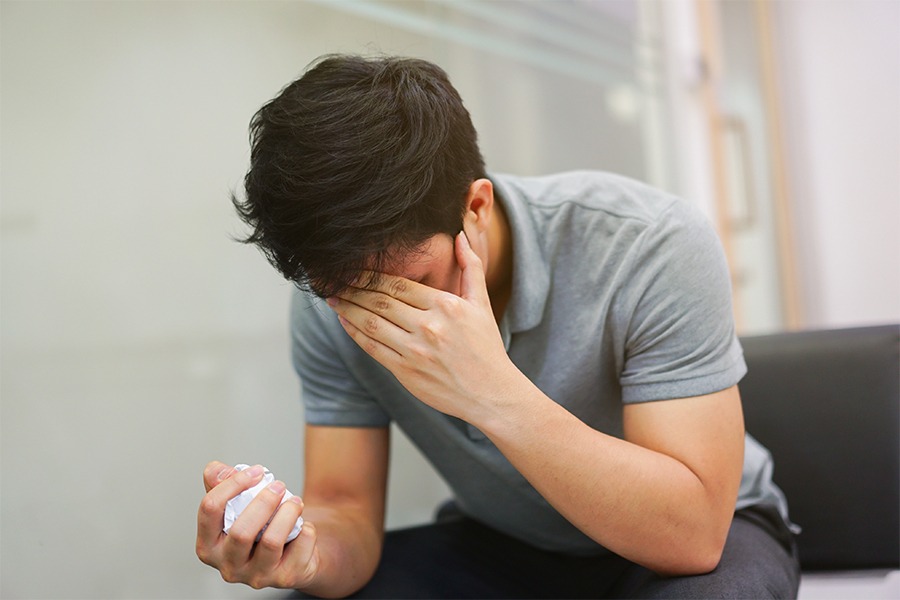 Man crying and shielding his face while sitting in grey chair in white office