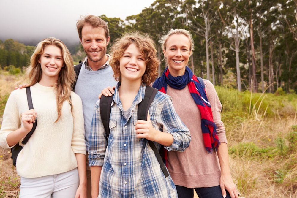 Group of a straight couple in their forties, a teenage woman, and a gender non-conforming child with the man's hand on their shoulder