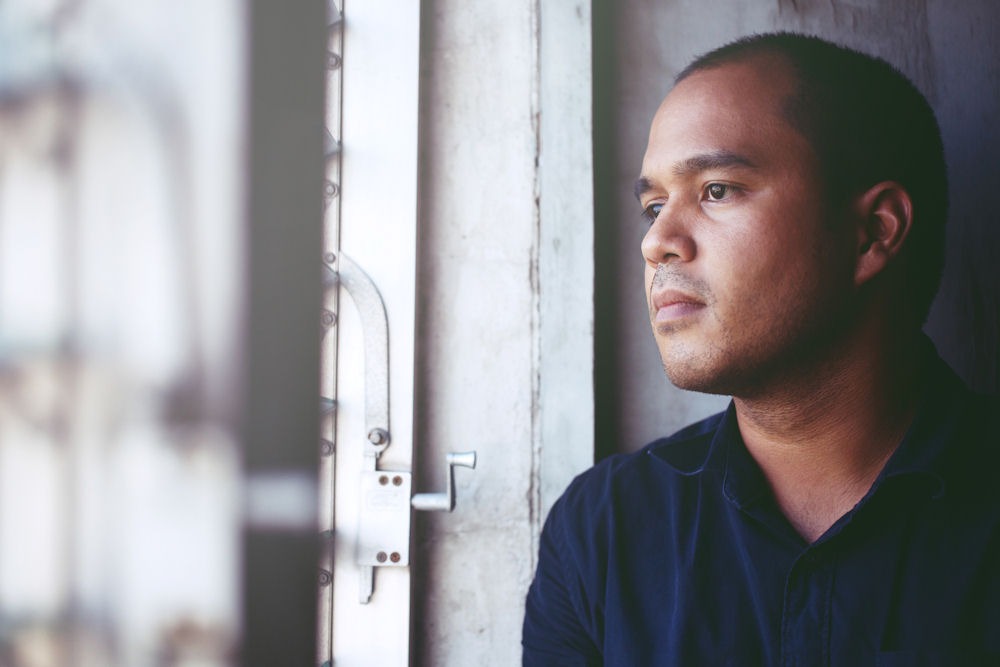 Thoughtful man looking out the open window of house painted white