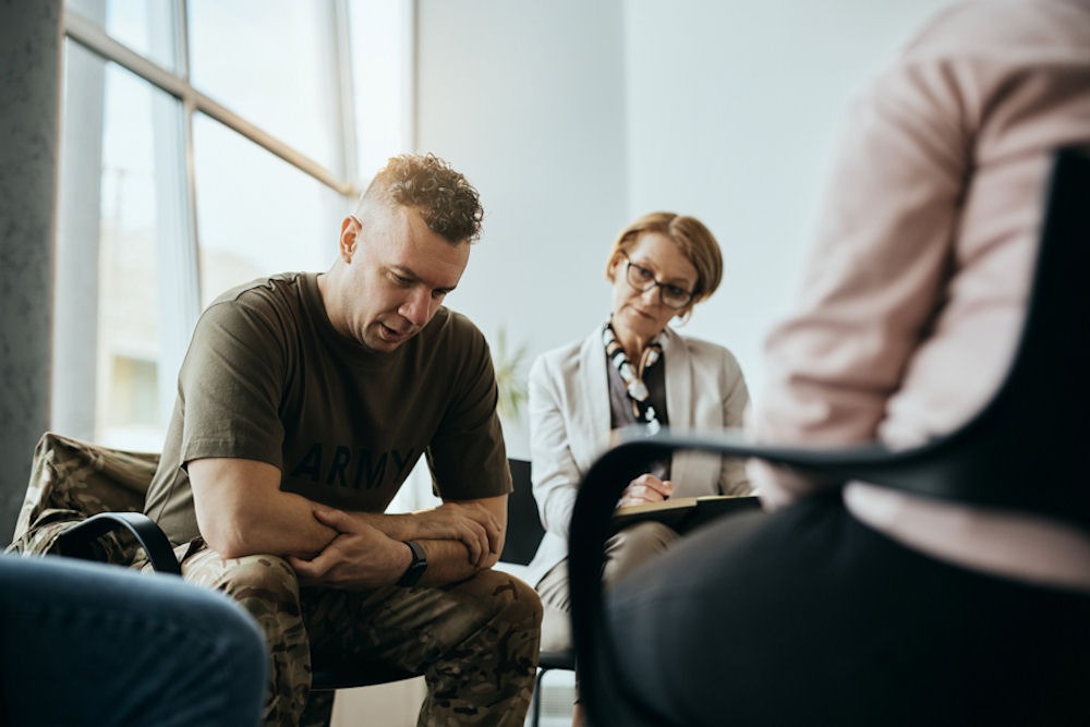 Man in combat fatigues shares personal story during family therapy session.