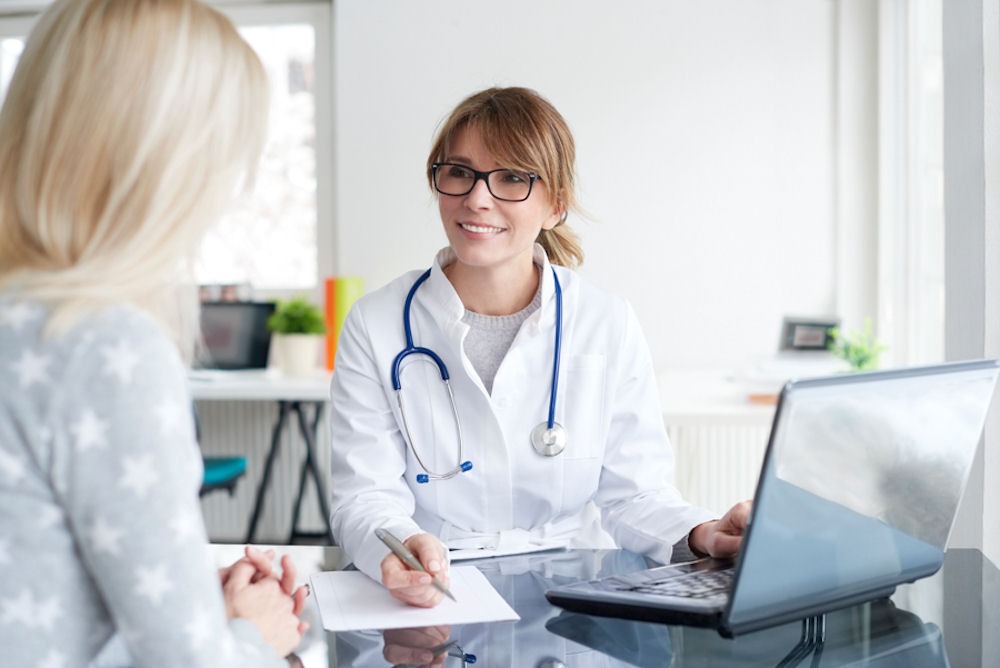 Doctor with stethoscope and laptop discussing alcohol intolerance and allergy with young woman