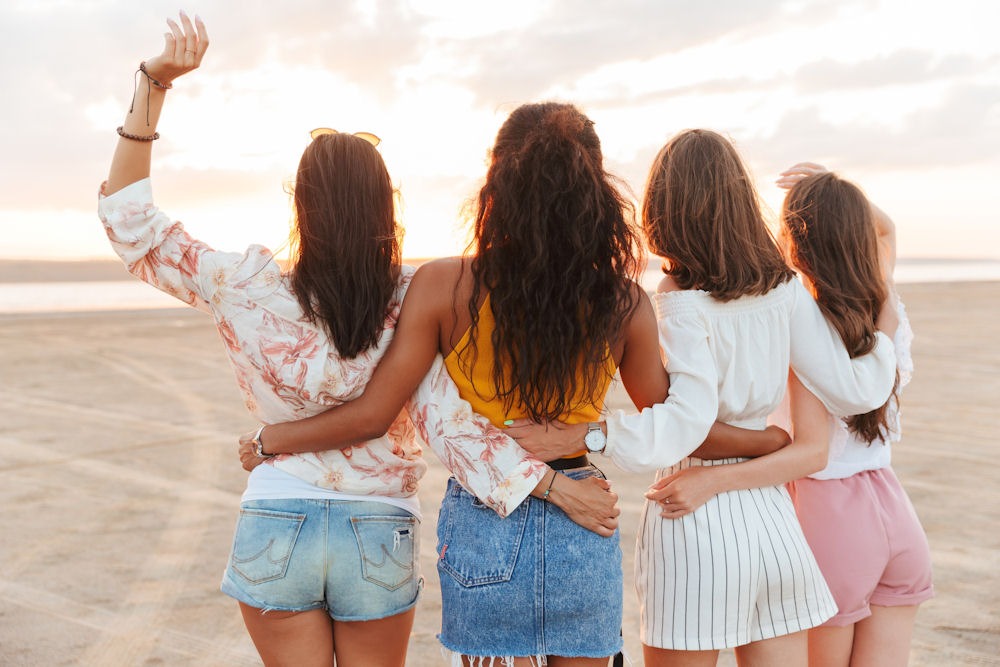 Four friends facing away from the camera while looking out onto the beach