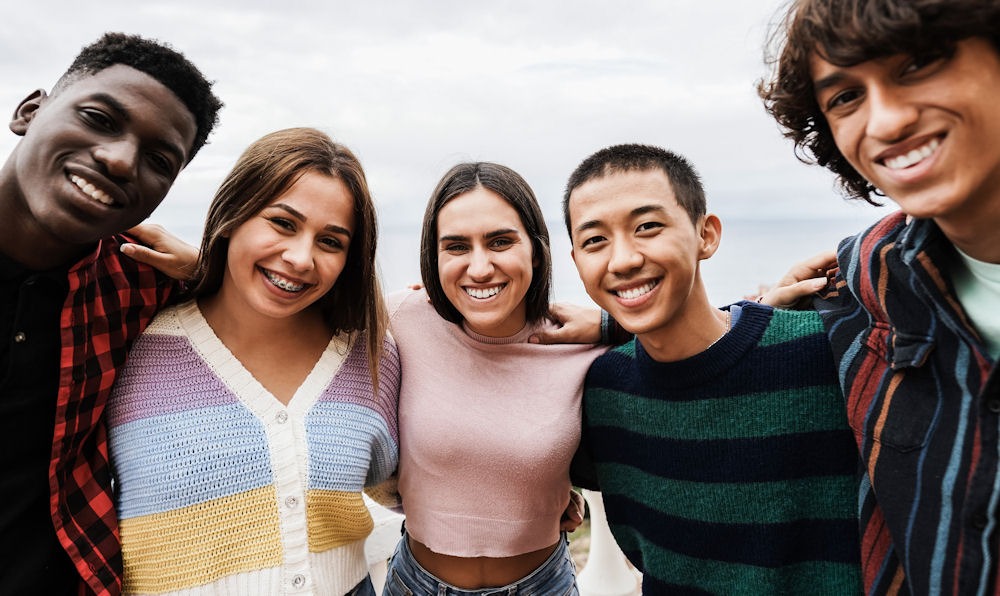 Group of three young men and two young women bracing shoulders while having fun at the beach