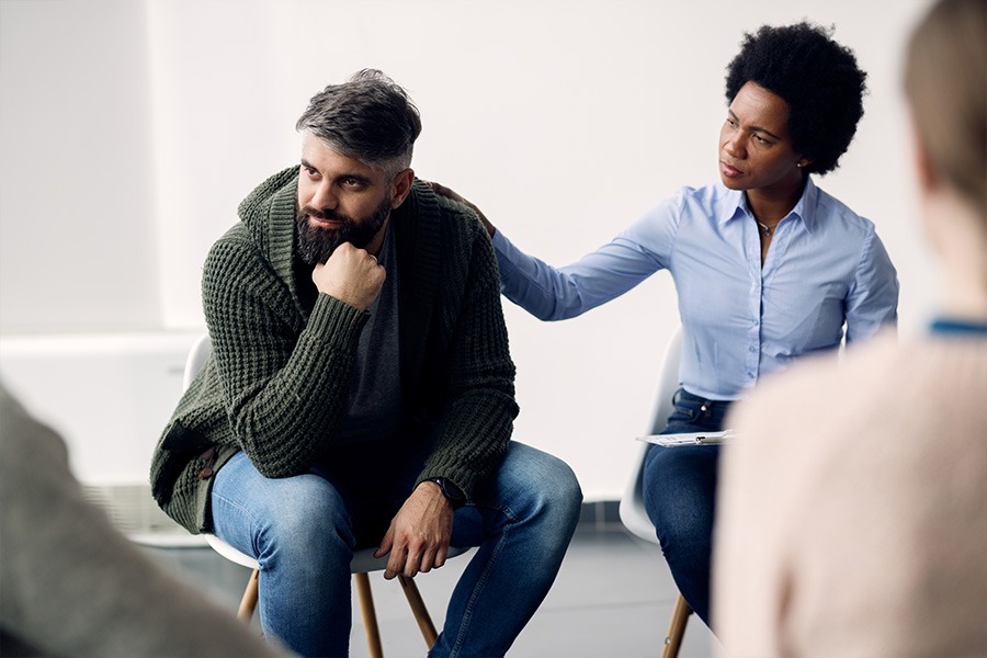 Woman reassuring man in group therapy about addiction withdrawal