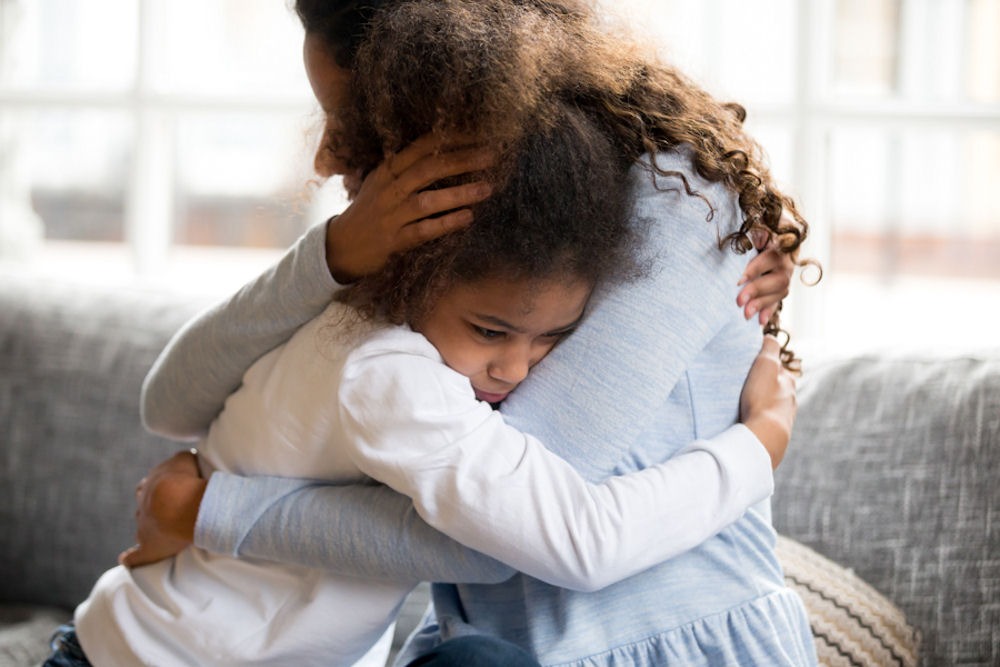 Woman embracing small, scared child on grey couch