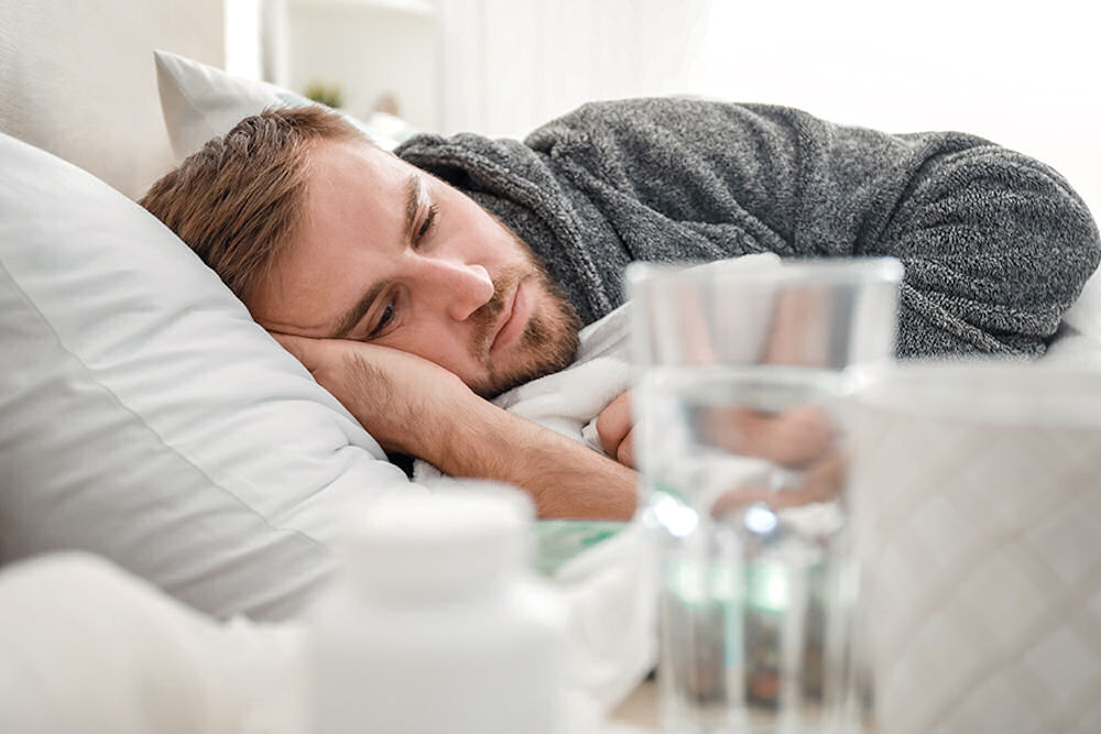 Man laying in bed with water and medication on the side table