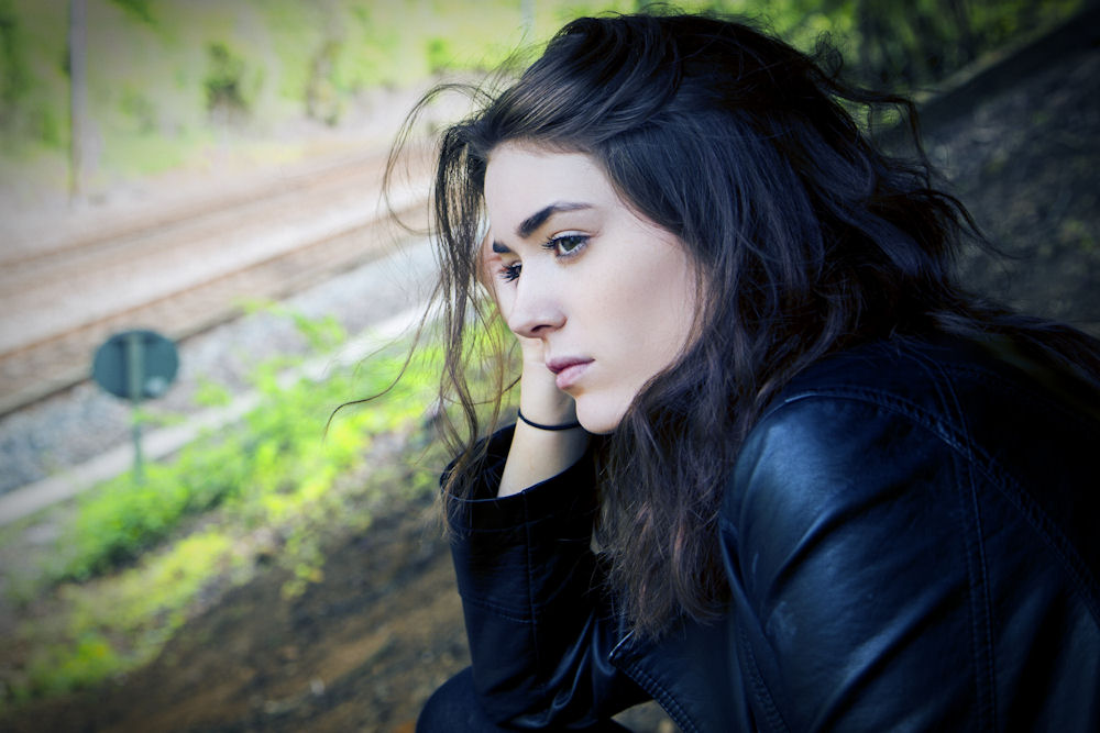 Woman contemplating her OCD sitting next to a tree overlooking a road