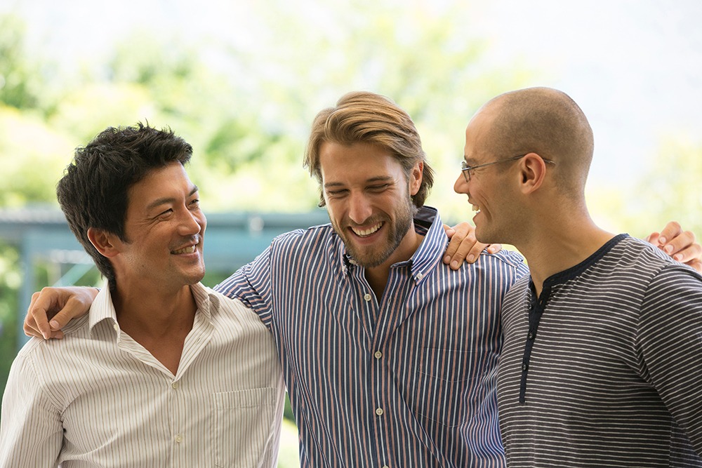 Three male friends smiling with their arms around each other.