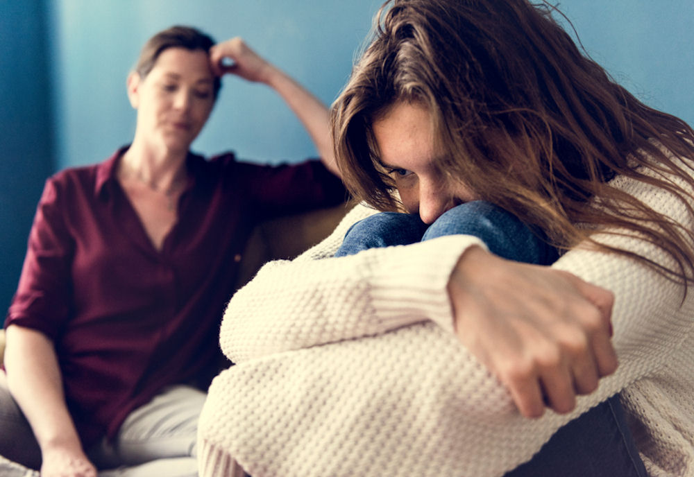 Frustrated woman talking to young addicted woman coiled into a ball