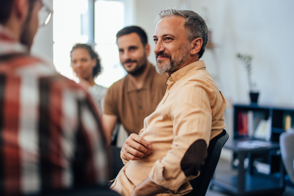 Man smiling while listening to people talk in 12 Step meeting