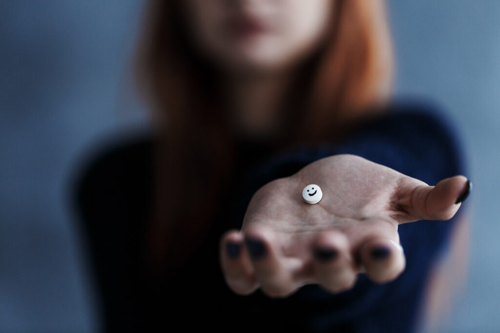 Woman holding out white Gabapentin pill with smiley face on it