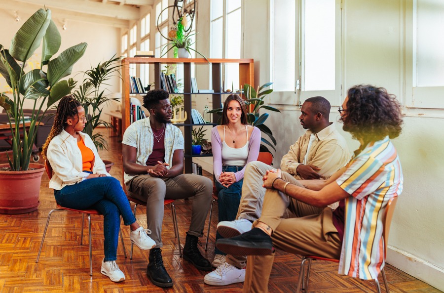 Gorup of five people in 12-step meeting in multi-use room full of plants